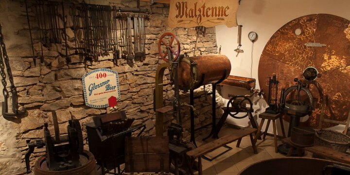 Historische Geräte einer alten Malztenne stehen vor einem Schild mit der Aufschrift "Glossner Bier" in einem Museum