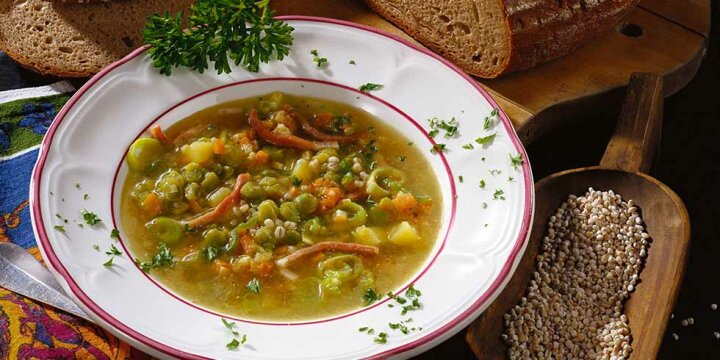 Suppe mit Erbsen und anderen Gemüsesorten sowie Speckwürfeln und Graupen, serviert in einem Suppenteller