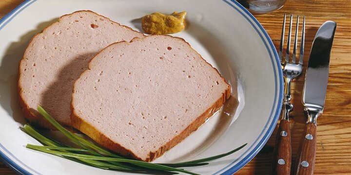 Zwei Scheiben Bayerischer Leberkäse mit etwas süßem Senf auf einem Teller angerichtet