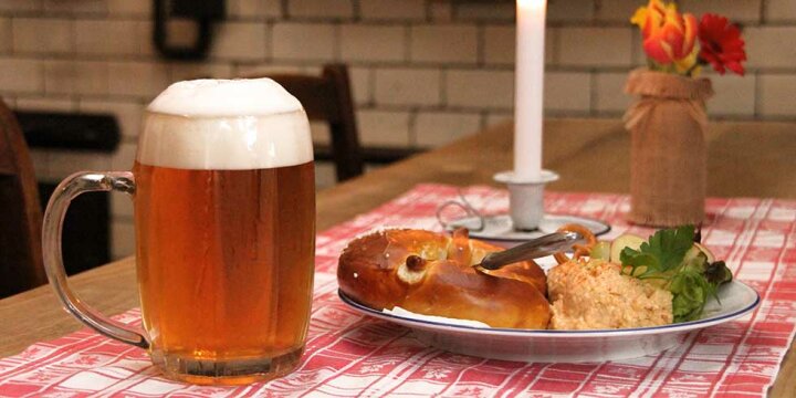 ein Glaskrug mit Zoigl auf einem Tisch mit Brotzeitteller, u.a. Breze und Obazda